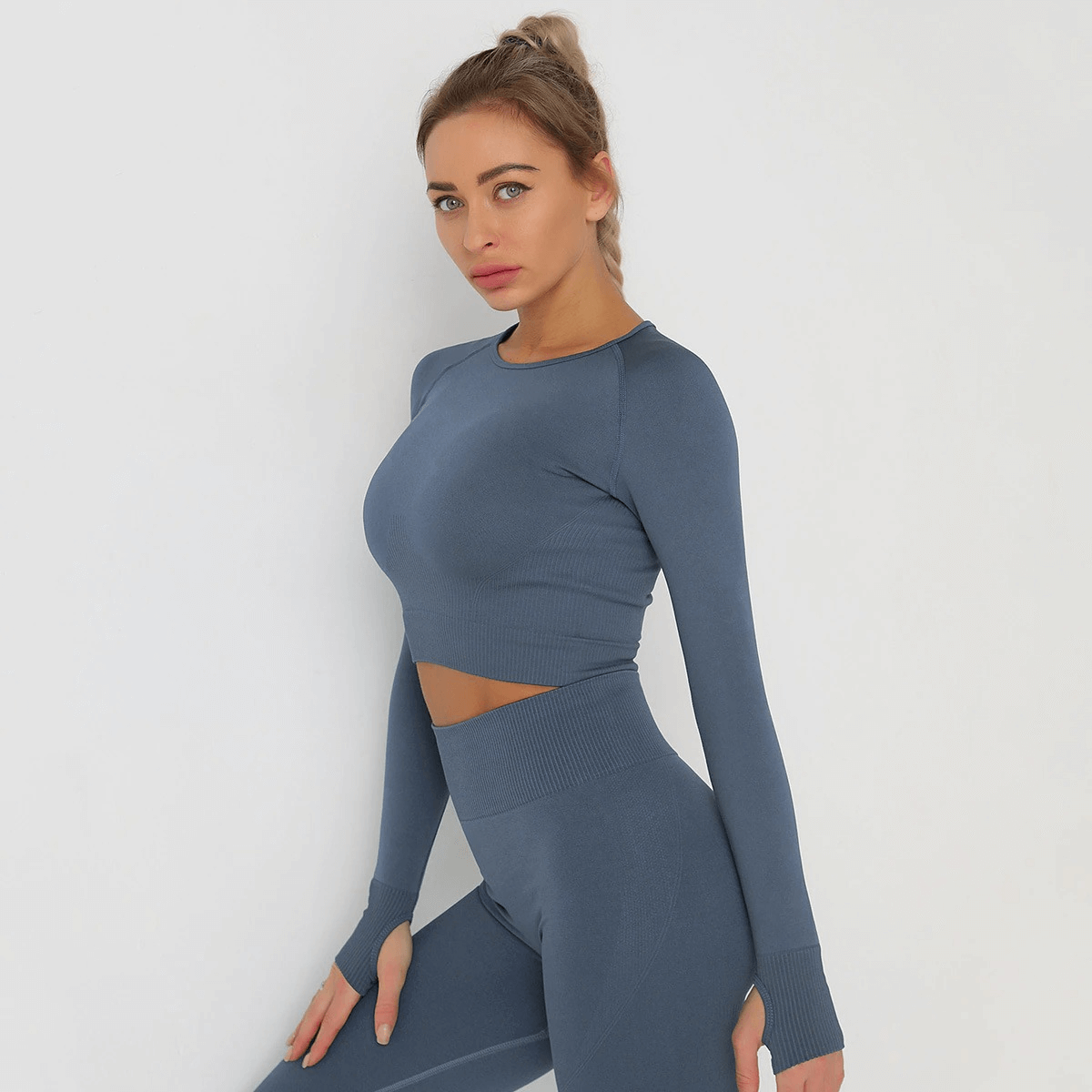 Model wearing a blue long sleeve crop top, perfect for yoga and running, made from breathable nylon and spandex, showcasing sporty fashion.